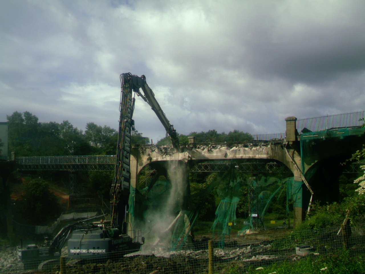 large cranes near small green trees under a cloudy sky