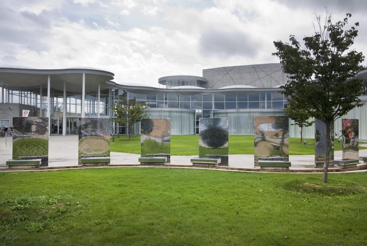 a circular lawn area with benches and plants and a tree