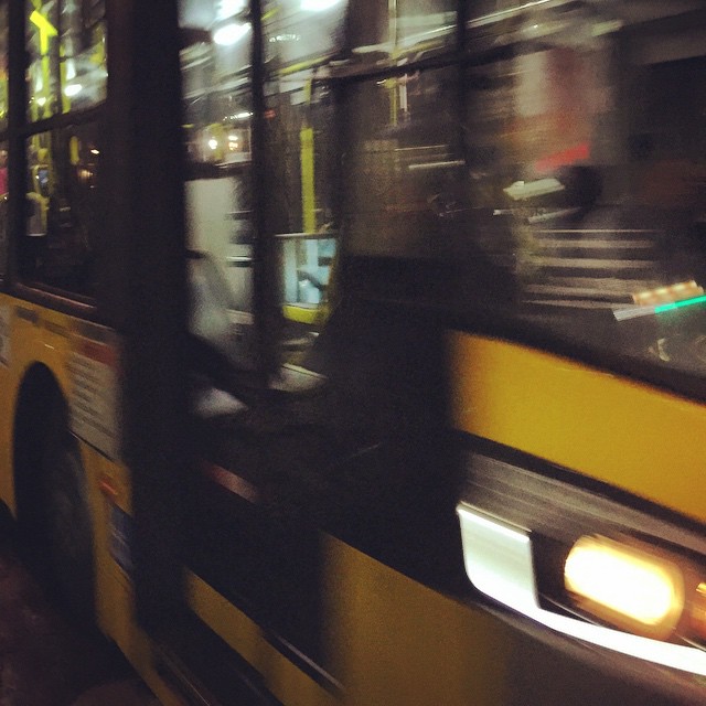 a yellow bus parked next to a sidewalk near a pole