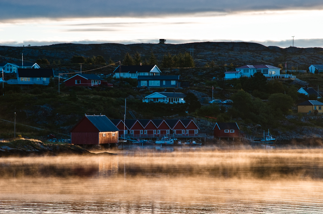 mist covers a lake with small houses on the hillside