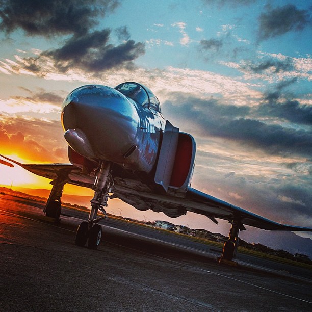 a jet airplane sitting on an airport runway with the sun going down