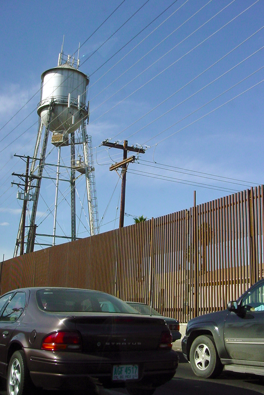 two cars are parked in front of a fence with a water tower on top