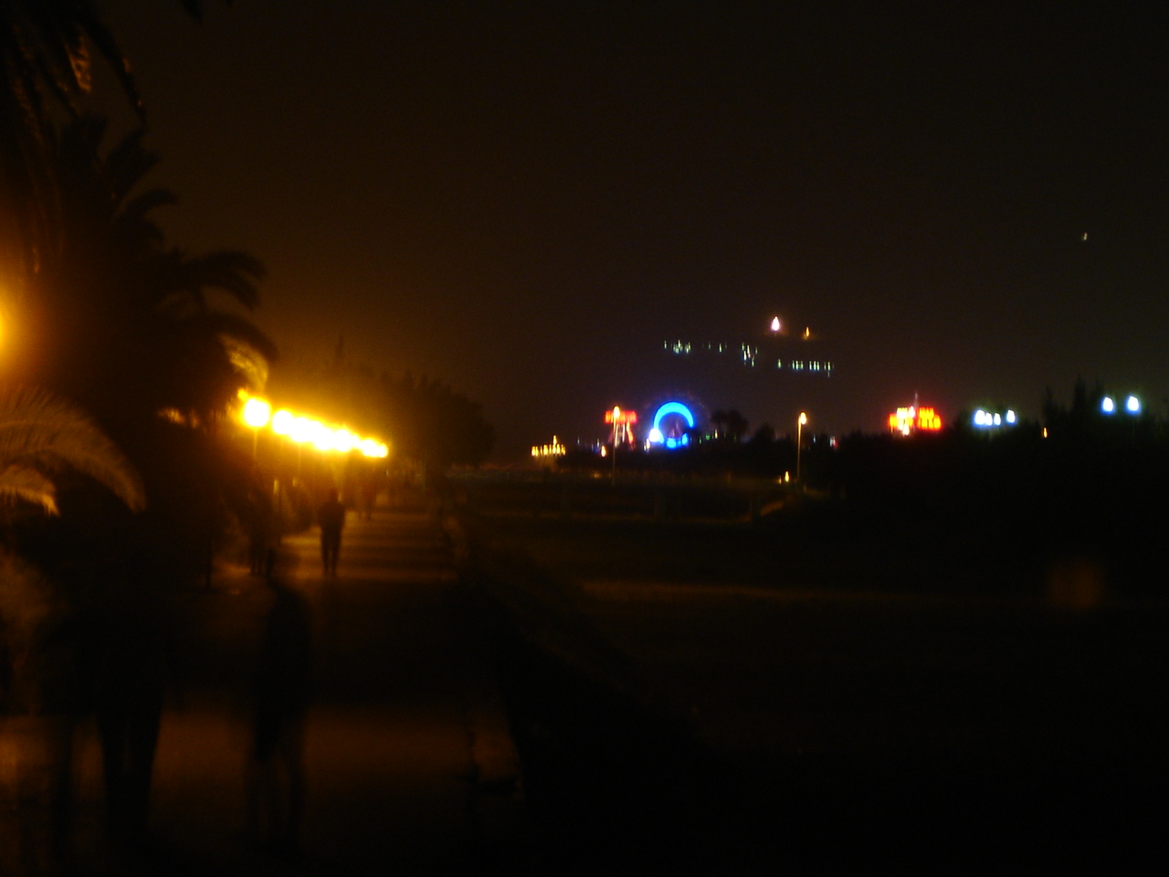 people walk along the sidewalk at night under the city lights