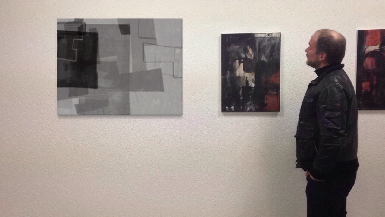 man in black jacket looking at two abstract paintings