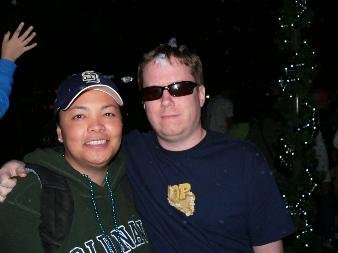 two people posing for the camera in front of a christmas tree