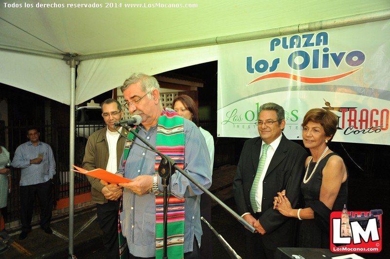 man speaking at podium with others under tent