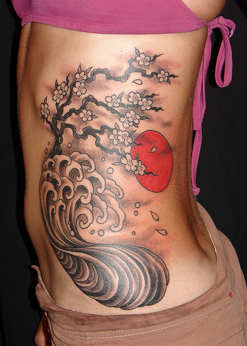 a woman's lower back tattoos has a cherry blossom and wave in the ocean