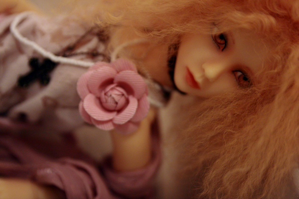 there is a beautiful doll laying down with a pink rose on her head