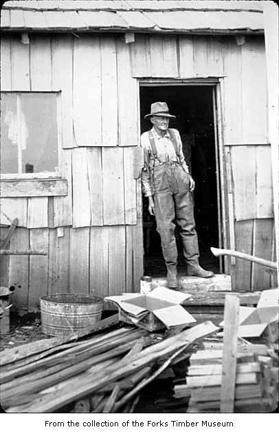 an old pograph of an man standing in the doorway of a shack