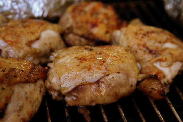 close up po of a chicken and other food cooking on a grill