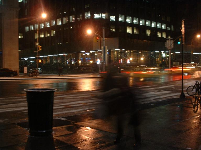 people walking on a street at night with an office building in the background