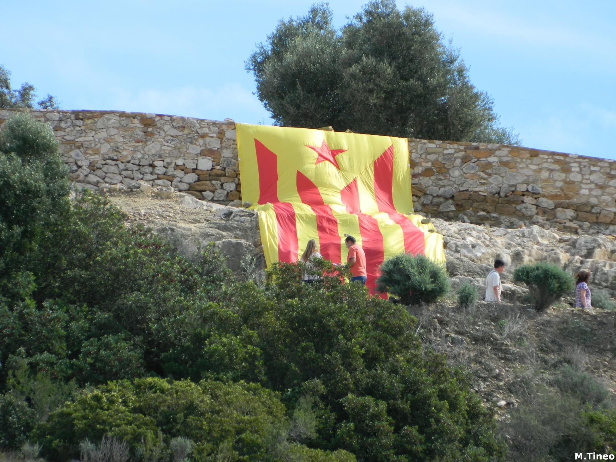 children stand in the foreground and watch an open fire safety banner hanging on the side of a rocky cliff