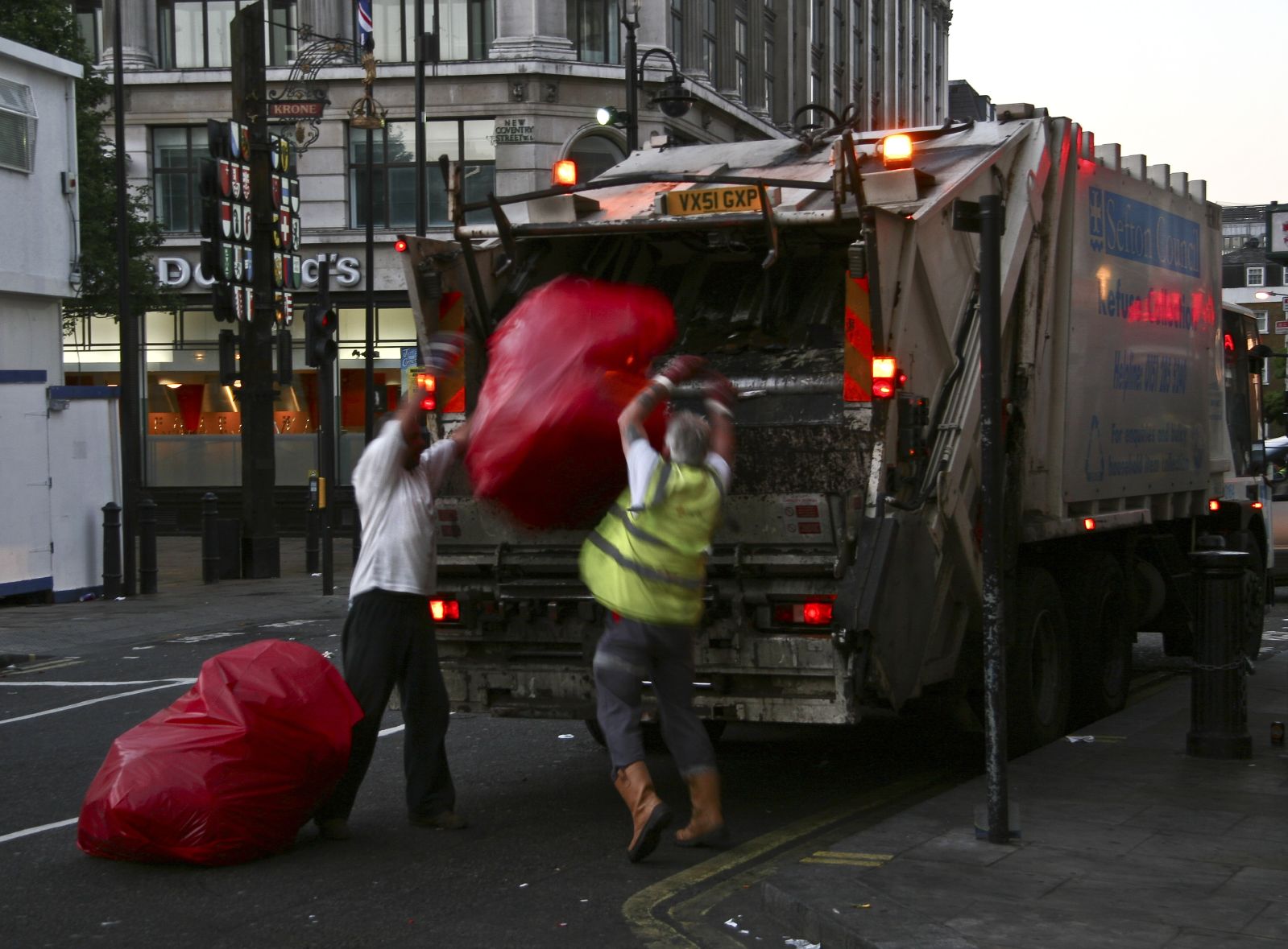 three men lifting a giant frisbee from the back of a garbage truck