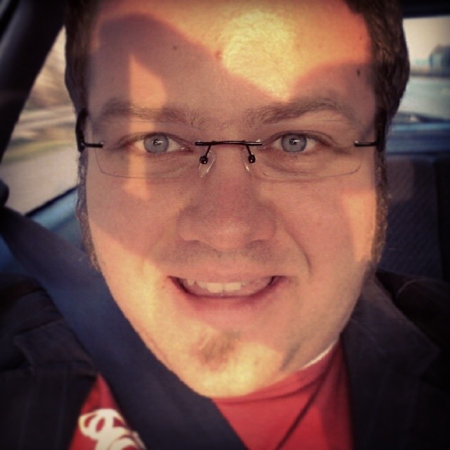 a man wearing glasses sitting in a car smiling