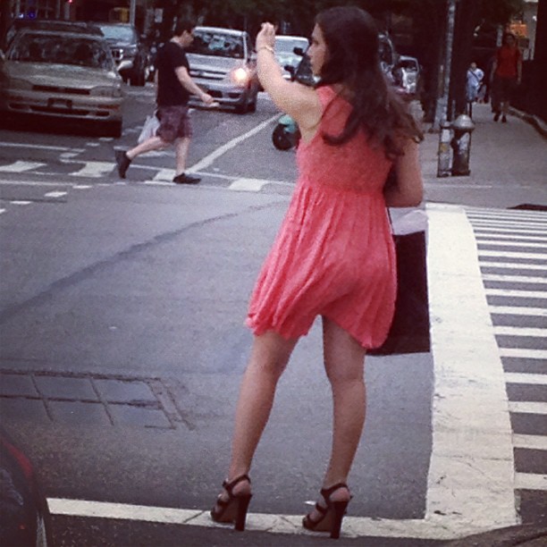 a woman in a pink dress standing on the street looking at traffic