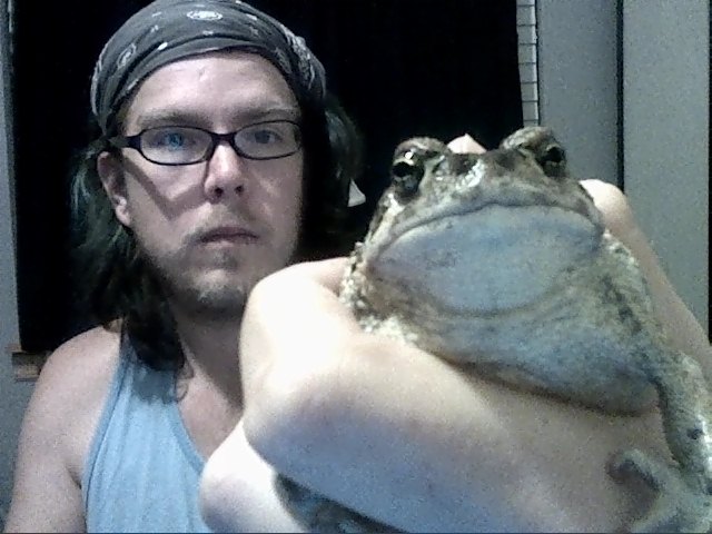 a man in a bandana holds a frog that appears to be very large