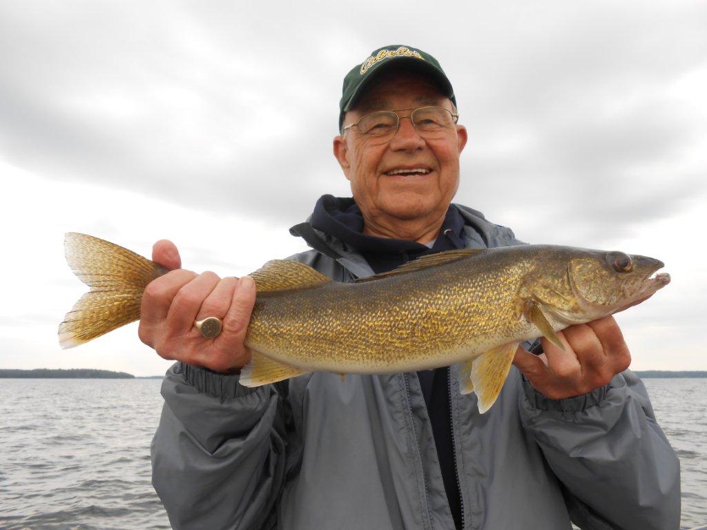 an older man holding up a large fish on the boat