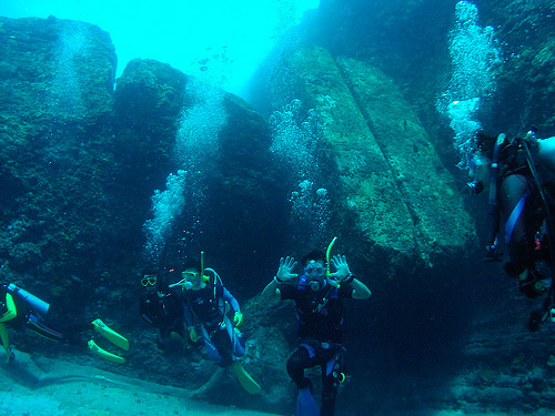 three scubas take pos of the underwater rock walls