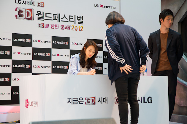 a person signing autographs while someone else looks on
