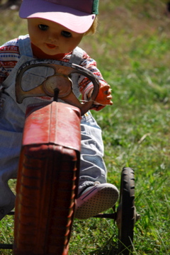 a doll sitting in the grass with a toy tractor