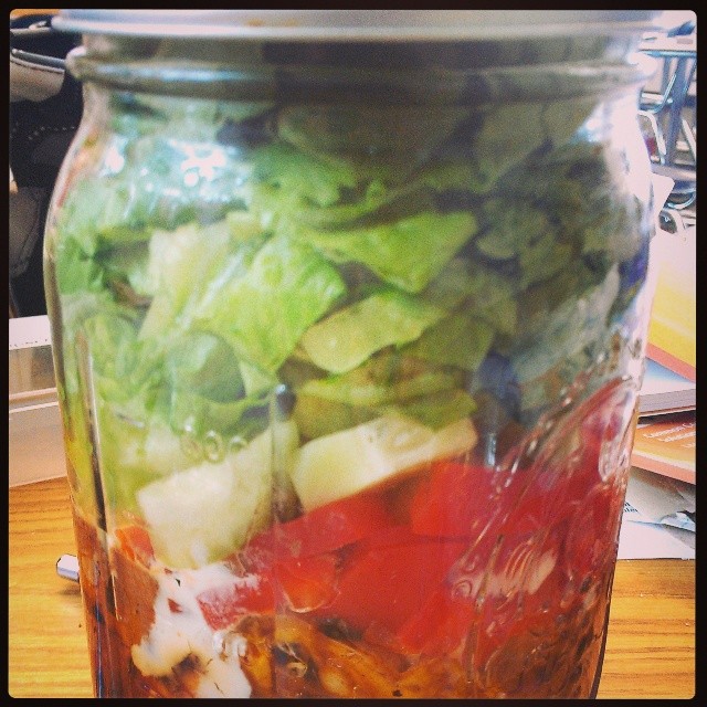 lettuce, tomatoes, and other vegetables are in a mason jar