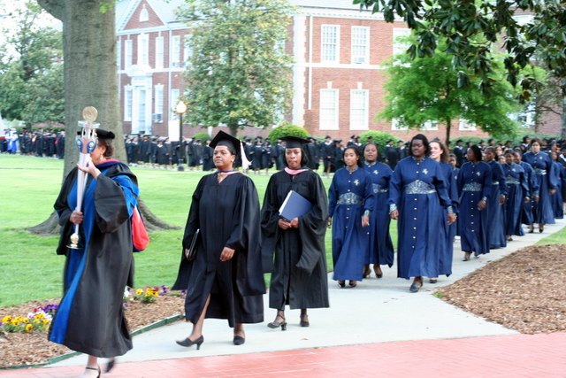 a group of students in graduation gowns and with diplomas walking down a sidewalk near a park