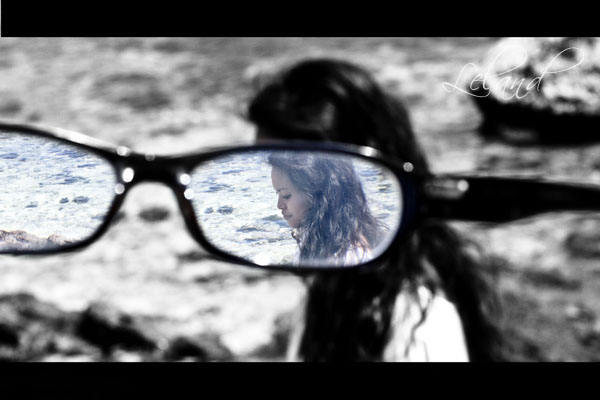 a woman looks in her sunglasses while reflected by the reflection of some rocks and water