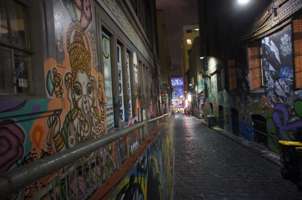 a narrow street at night with a few people walking down it