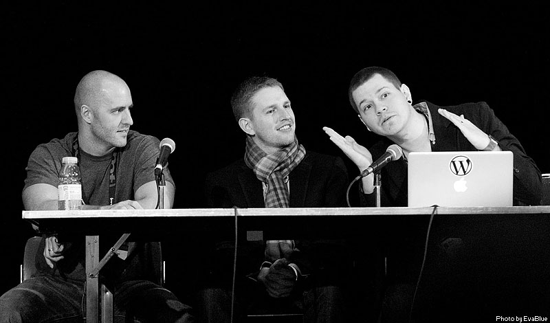 five men are sitting on a panel and the man is wearing a jacket