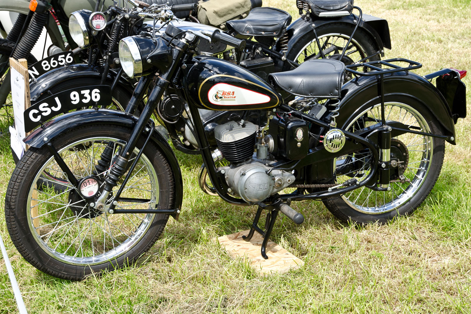 two old style motorcycles are parked in a grassy area