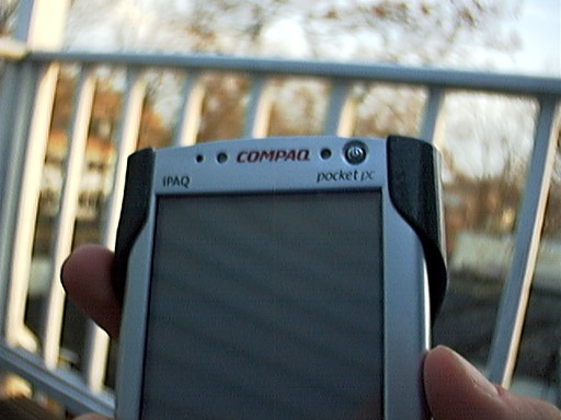 the hand is holding a mobile phone in front of a railing