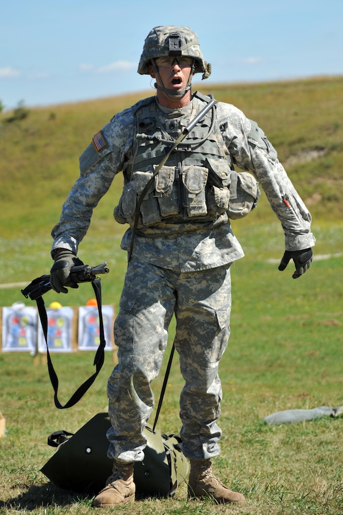 a soldier in full camouflage holding a pole and hat