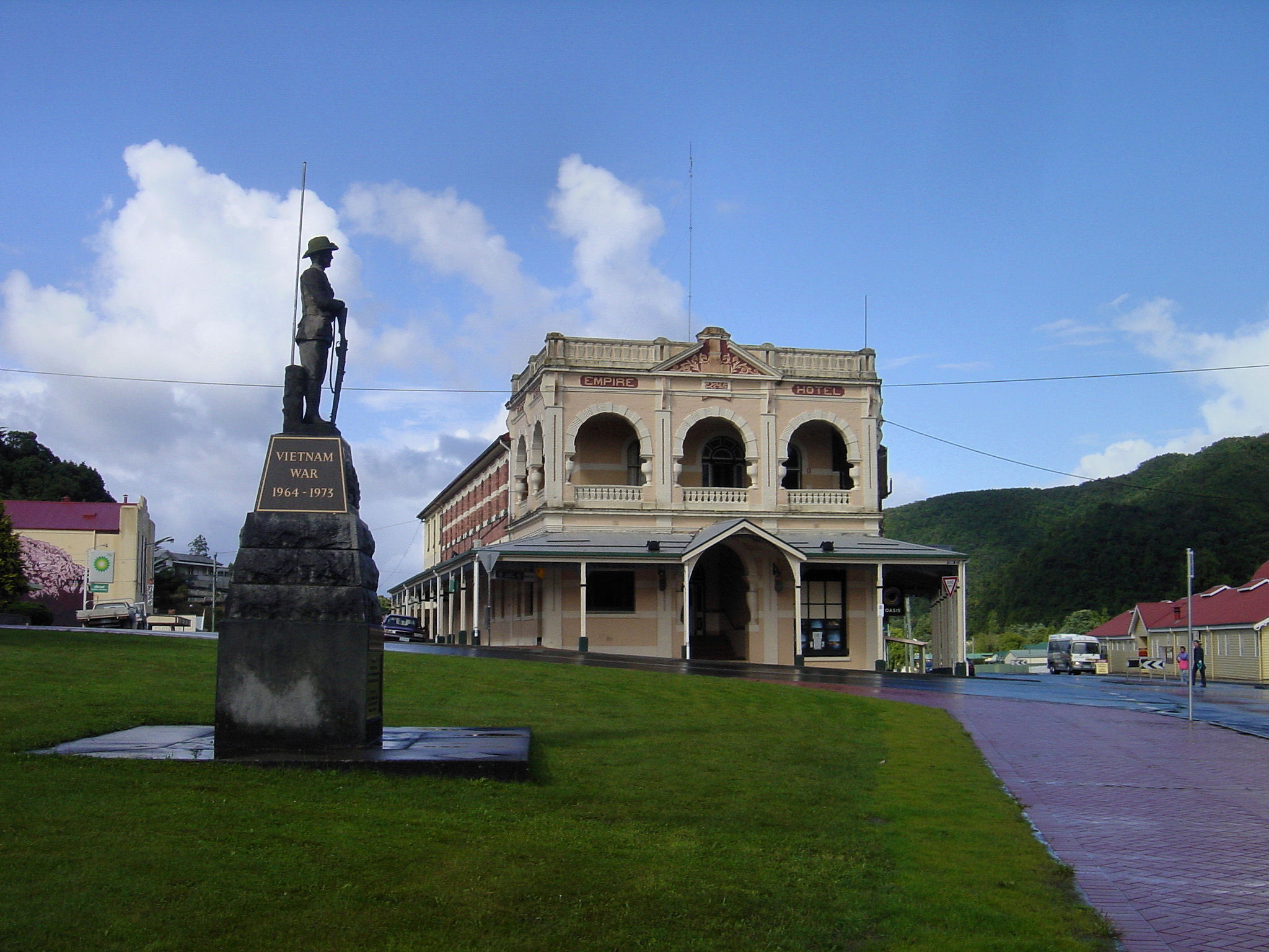 an old statue stands on a grassy lawn near a small town with lots of buildings