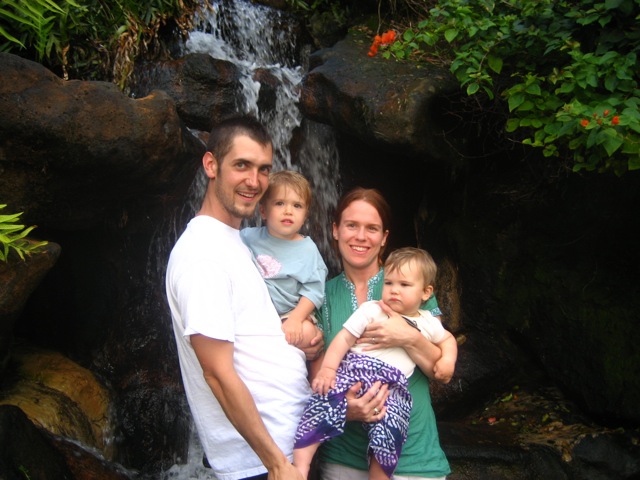 a family of five stand in front of a waterfall with an infant girl