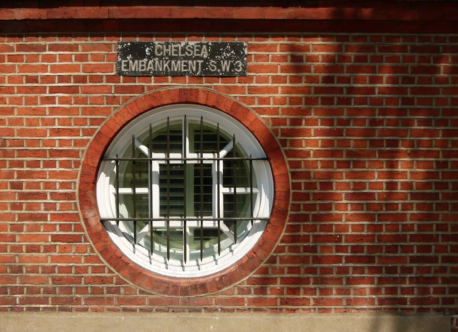 a brick wall with a round window and sign for chelsea park, on it
