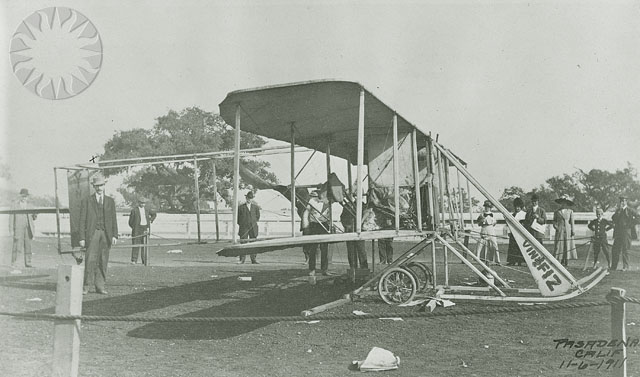 an old biplane is broken open while a group stands around