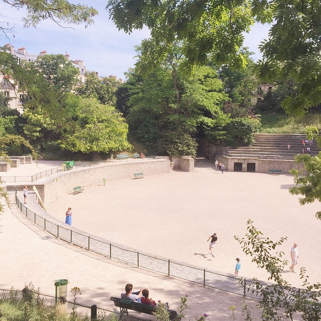 three people are sitting at a public bench in a park