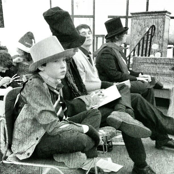 two boys are seated on a bench with hats on their heads