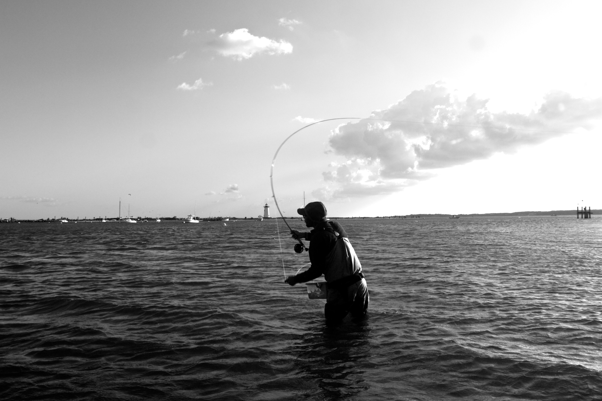 a man with a hat and long fish rod wades in a body of water