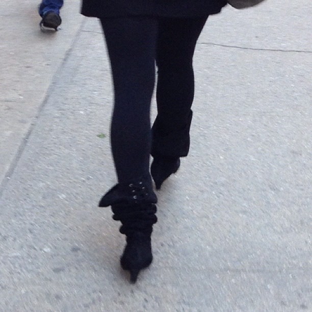 a woman in a black jacket and black pants walking down a street
