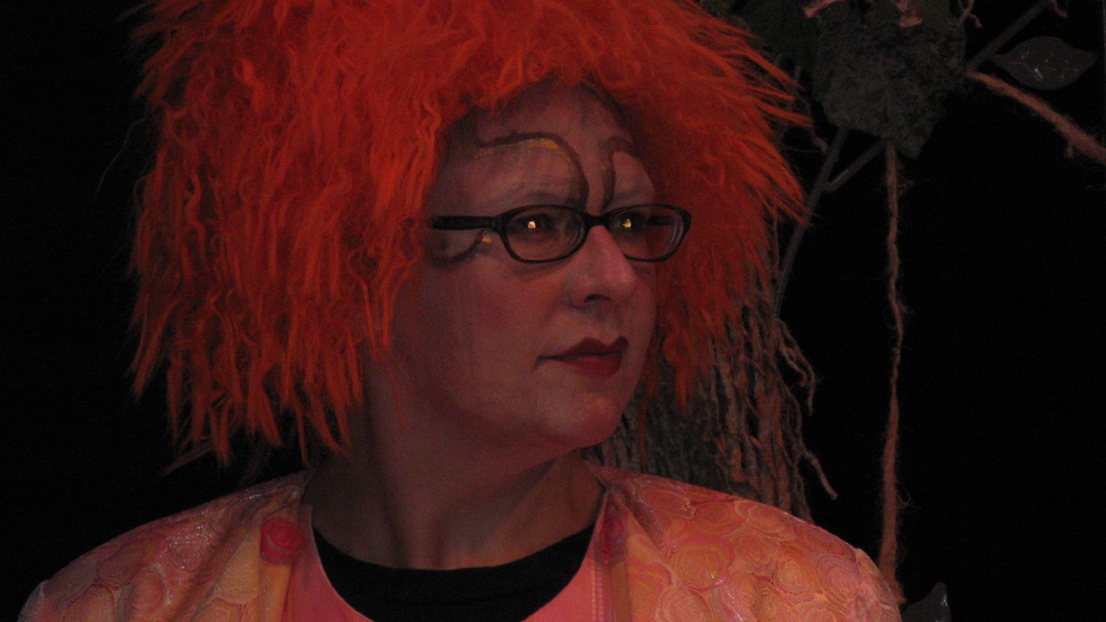 a woman with bright red hair and glasses stares ahead