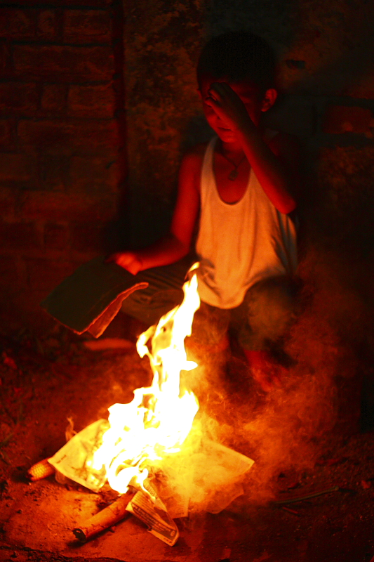 a boy sitting on a bench next to a fire