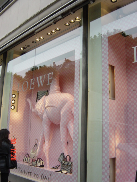 this window has pink checkerboard and is featuring a white mannequin wearing a horse in its mouth