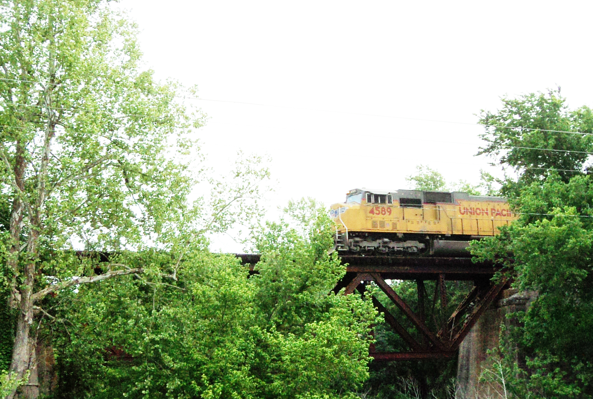 a yellow train riding on the tracks over a bridge