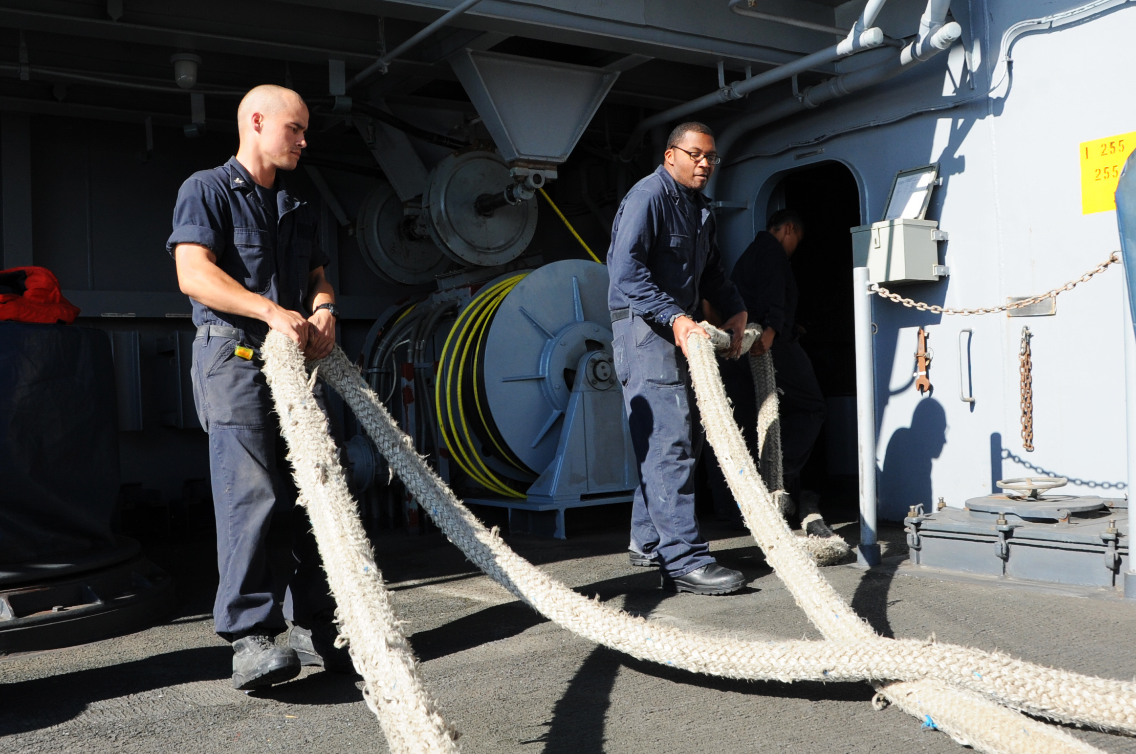 two sailors are hanging a large rope on a ship