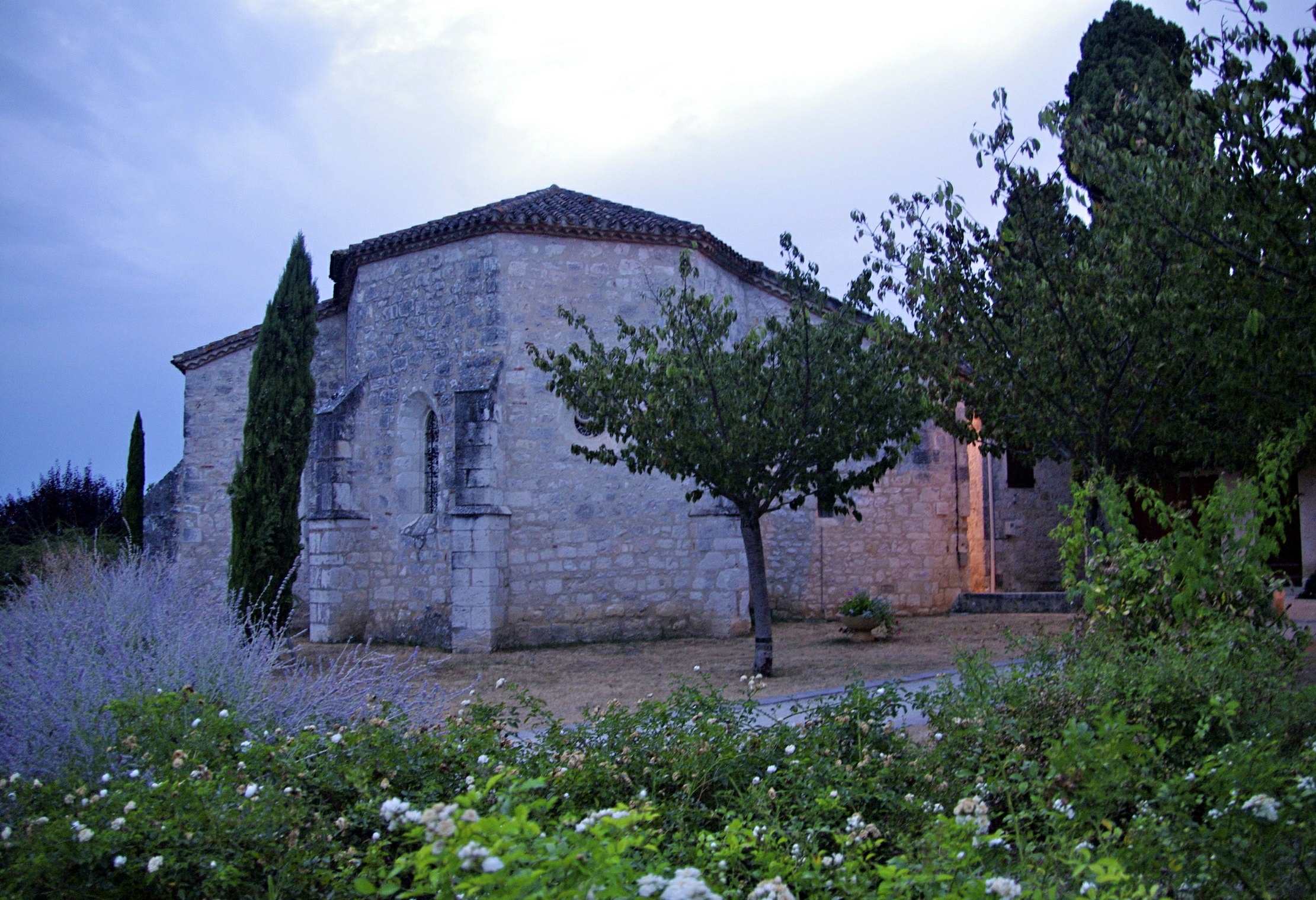 an old stone building surrounded by trees and flowers