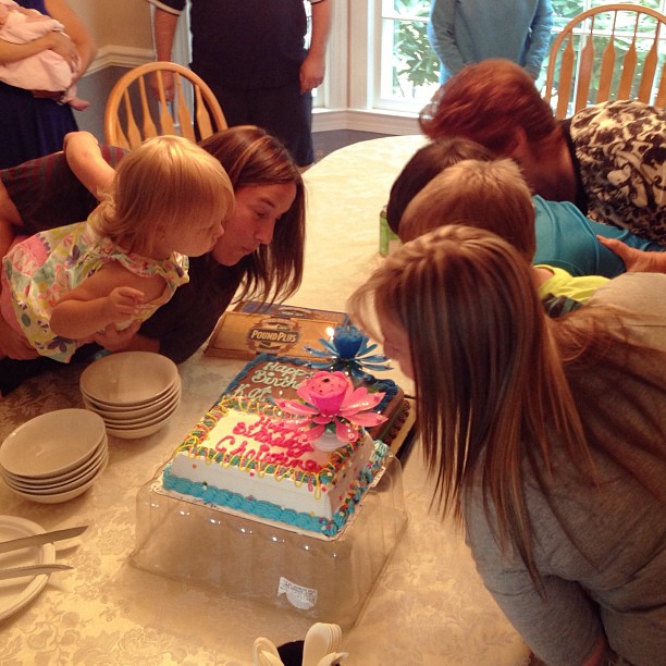 woman and three girls blowing out candles on a birthday cake