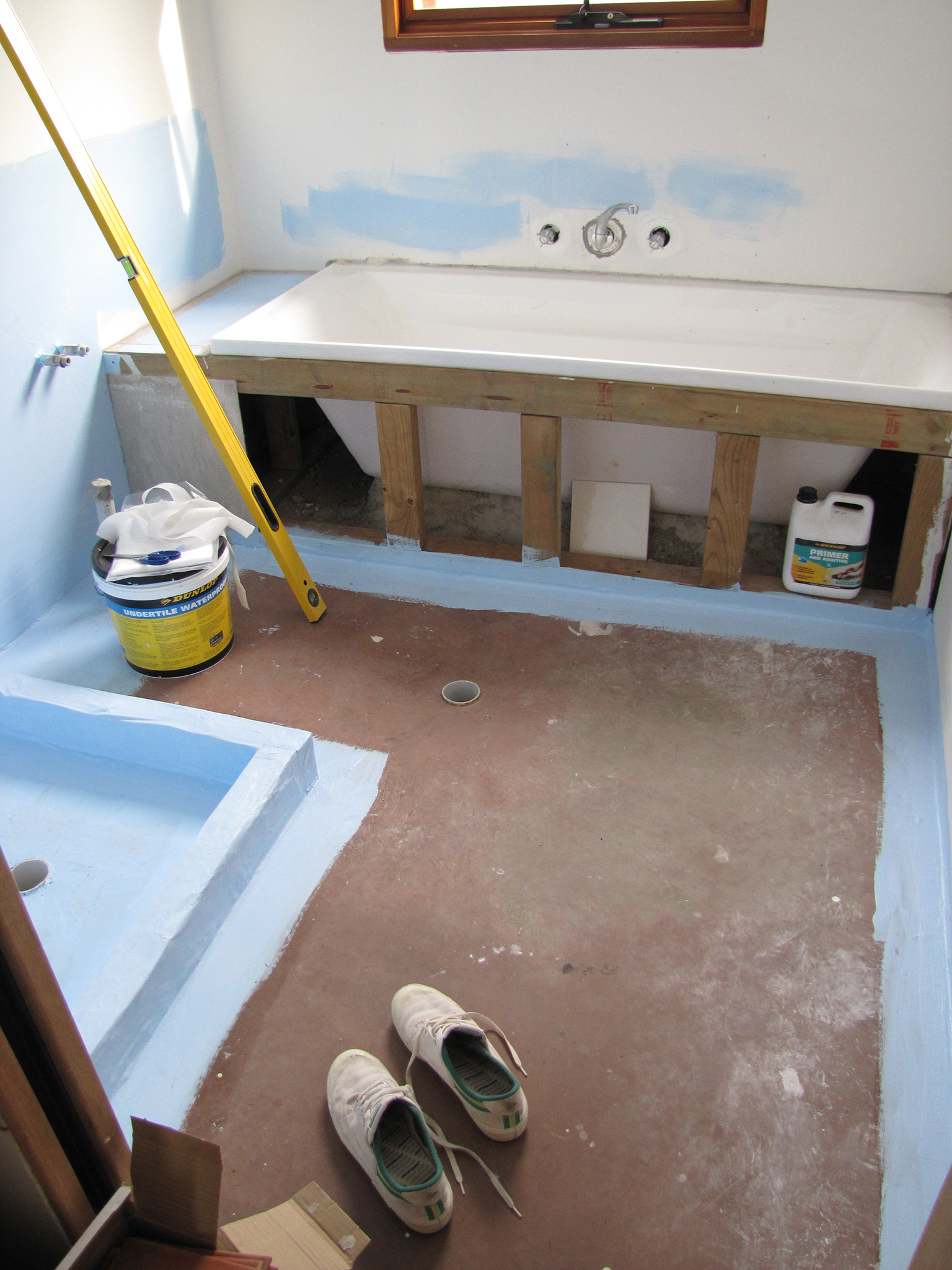 a bathroom with paint, an unfinished tub and shoes on the floor