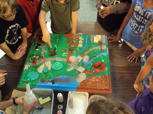 children are gathered around a large, green, paper - mache game