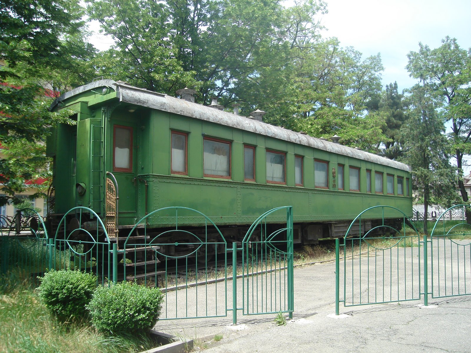 a green train car sitting on the tracks next to a fence